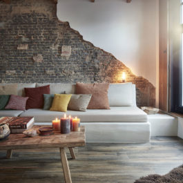 magnifique salon avec un canapé blanc, un mur en briques et un sol vinyle BerryAlloc. L'ambiance est réchauffée par de nombreuses bougies posées sur une table basse en bois